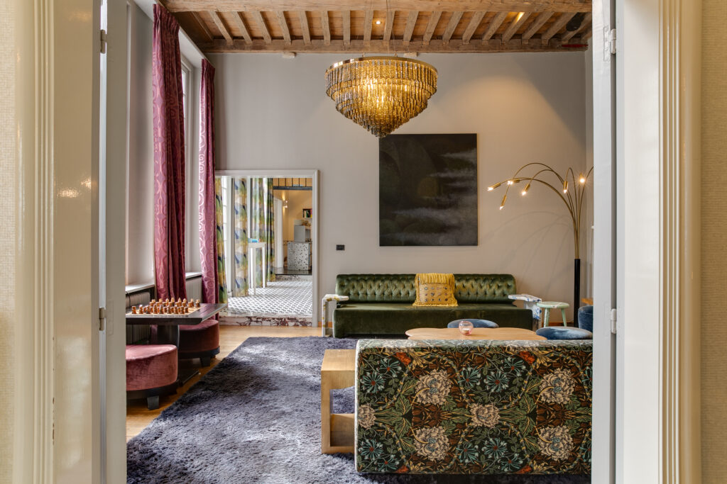 Elegante salón con sofá de terciopelo y lámpara de araña en hotel boutique de Amberes